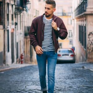man in maroon zip-up jacket walking near building